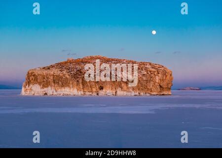 Fantastischer Sonnenuntergang mit Blick auf die Insel und den Mond im Winter auf dem Eis des Baikalsees, Sibirien Russland. Wintersaison Naturlandschaft. Speicherplatz kopieren. Stockfoto