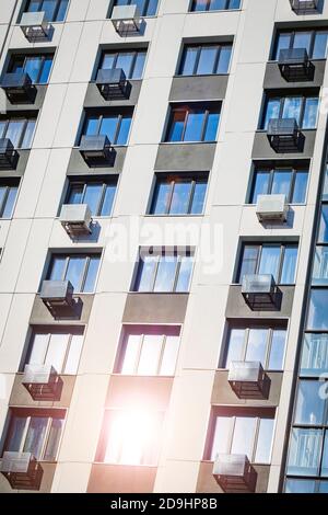 Fassade des Gebäudes mit Klimaanlagen. Sonnenlicht reflektiert im Fenster, vertikale Ansicht. Stockfoto