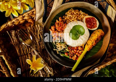 Nasi Campur Bali. Balinesische Mahlzeit mit Reis mit geschreddertem Huhn, Gemüsesalat, Erdnüssen, Satay, Ei und gebratenen Nudeln. Stockfoto
