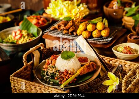 Nasi Campur Bali. Balinesische Mahlzeit mit Reis mit geschreddertem Huhn, Gemüsesalat, Erdnüssen, Satay, Ei und gebratenen Nudeln. Stockfoto