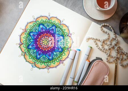 Draufsicht auf farbige Mandala Kunstbuch mit bunten Markern, Stift, rosa Stiftetui und Rosenkranz Perlen. Stockfoto