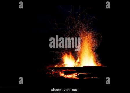 Schönes Lagerfeuer mit roten, gelben und orangenen Flammenausbreitung und Funken in Form von Tracks auf schwarzem Hintergrund Stockfoto