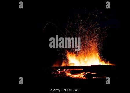 Schönes Lagerfeuer mit roten, gelben und orangenen Flammenausbreitung und Funken in Form von Tracks auf schwarzem Hintergrund Stockfoto