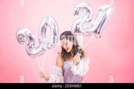 Happy junge Mädchen in festlichem Outfit auf rosa Studio Hintergrund Posing hält silberne Ballons aus 2021 Zahlen Stockfoto