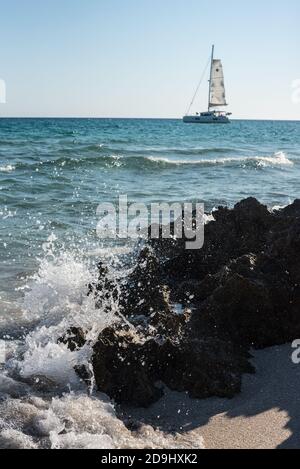Seascape mit Wellen brechen am Ufer gegen einige Felsen, und ein Boot im Hintergrund. Stockfoto