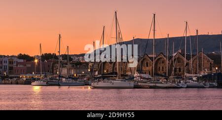Sonnenaufgang über dem alten venezianischen Hafen und Hafen von Chania, Kreta, Griechenland. Segelboote, Pier, alte venezianische Werften und entfernte kretische Berge. Stockfoto