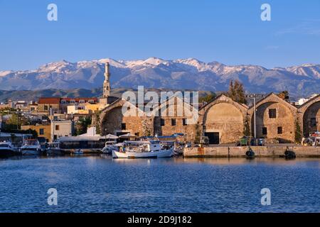 Fischerboote, die von Piers der alten venezianischen Werften oder Neoria verankert sind. Kirchturm und Minarett, entfernter kretischer Berg. Chania, Kreta, Griechenland. Stockfoto