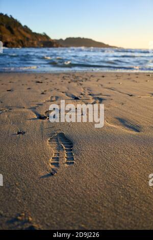 Schuhspuren und Fußabdrücke an einem Sandstrand führen zum Wasser an der Pazifikküste in Mendocino, Kalifornien. Stockfoto