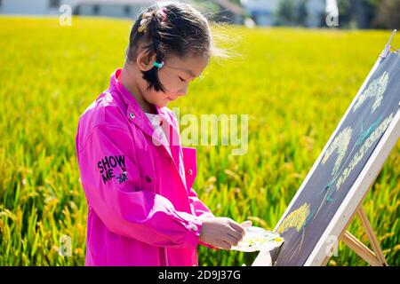 Eine Kindergärtnerin nimmt Kinder mit, um in den goldenen Reisfeldern zu malen, um den kommenden Herbst in Rugao City, der ostchinesischen Provinz Jiangsu, zu begrüßen. Stockfoto