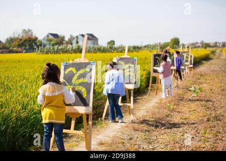 Eine Kindergärtnerin nimmt Kinder mit, um in den goldenen Reisfeldern zu malen, um den kommenden Herbst in Rugao City, der ostchinesischen Provinz Jiangsu, zu begrüßen. Stockfoto