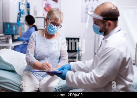 Ältere Patienten unterzeichnen medizinische Vereinbarung der Testergebnisse tragen Schutzmaske gegen covid Pandemie im Krankenhaus. Medizinische Arztkonsultation während der globalen COVID-19-Krise. Stockfoto