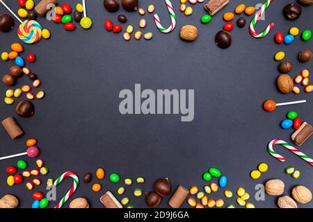 Verschiedene Süßigkeiten, Lutscher, Bonbons, Marmelade, Walnüsse, Kastanien auf schwarzem Hintergrund. Festliche Komposition. Hintergrund für das Essen Stockfoto