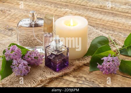 Parfümflaschen, brennende Kerze und Fliederblumen auf Sacktuch und alten Holzbrettern. Stockfoto