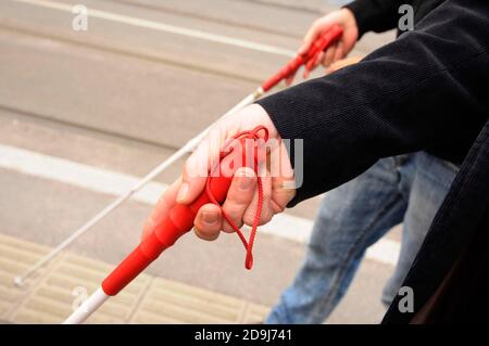 Menschen halten weiße Stöcke mit roten Griffen und gehen weiter Die Straße Stockfoto