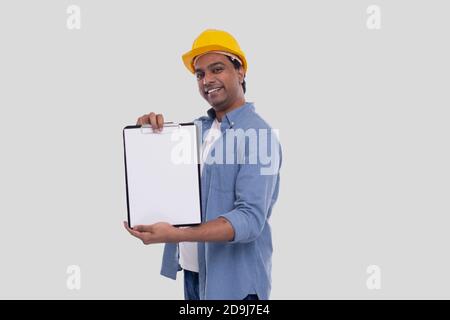 Bauarbeiter zeigt die Zwischenablage mit gelbem HardHat. Isoliert Stockfoto