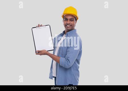 Bauarbeiter zeigt die Zwischenablage mit gelbem HardHat. Isoliert Stockfoto