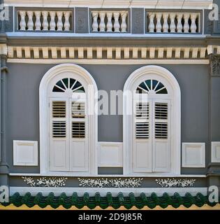 Restauriertes graues traditionelles peranakan-Gebäude mit zwei verzierten weißen Bogenfenstern. Stockfoto