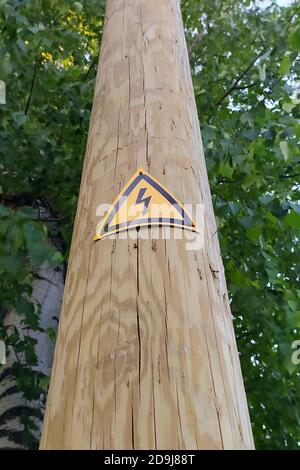 Zeichen der Gefahr eines elektrischen Schlags auf einem Holzmast. Schwarzer Blitz gegen ein gelbes Dreieck. Stock Foto mit leerem Platz für Text und Design. Stockfoto