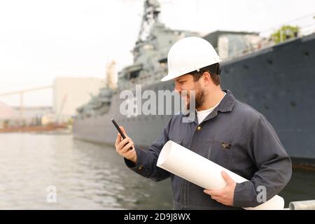 Marine DDE, designierter diensthabender Ingenieur, im Gespräch mit VHF-Walkie-Talkie, mit Papieren in der Nähe des Schiffes im Hintergrund. Stockfoto