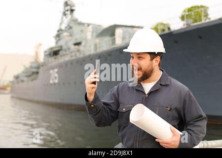 Marine Assistant Engineer hält VHF Walkie Talkie und Papiere in der Nähe des Schiffes im Hintergrund. Stockfoto