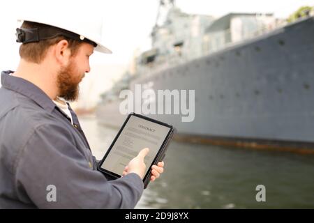 Kapitän im Helm Lesevertrag auf Tablette in der Nähe von Schiff im Hintergrund. Stockfoto