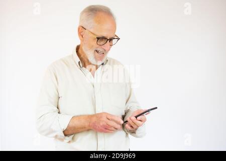 Studioaufnahme eines glücklichen älteren bärtigen Geschäftsmannes, der während des Einsatzes lächelte Handy mit Brillen vor weißem Hintergrund Stockfoto