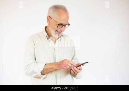 Studioaufnahme eines glücklichen älteren bärtigen Geschäftsmannes, der während des Einsatzes lächelte Handy mit Brillen vor weißem Hintergrund Stockfoto