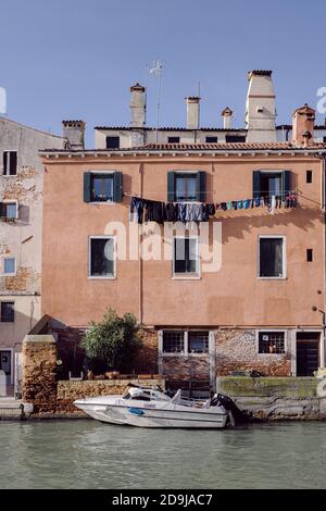 Hohe Außenfassade mit orangefarbener Wand, festgefestertes Boot auf einem Venedig-Kanal Stockfoto