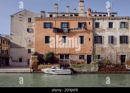 Hohe Außenfassade mit orangefarbener Wand, festgefestertes Boot auf einem Venedig-Kanal Stockfoto