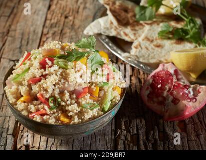 Gemischter Couscous- und Quinoa-Salat mit Granatapfel und buntem Süßes Paprika auf einem rustikalen Holztisch hoch Winkel betrachtet Stockfoto