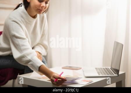 Komfortabel. Frau Schreiben Brief, Grußkarte für Neujahr und Weihnachten 2021 für Freunde oder Familie sitzen zu Hause mit Laptop. Feiertage, Feier. Sieht fröhlich, glücklich, vorsichtig aus. Stockfoto