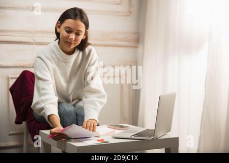 Komfortabel. Frau Schreiben Brief, Grußkarte für Neujahr und Weihnachten 2021 für Freunde oder Familie sitzen zu Hause mit Laptop. Feiertage, Feier. Sieht fröhlich, glücklich, vorsichtig aus. Stockfoto