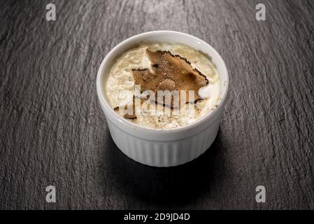 Gebackenes Ei und ​​fontina-Käsefondue mit geschnittenen Trüffeln in Kokotte, auf einer schwarzen Schiefersteinoberfläche Stockfoto