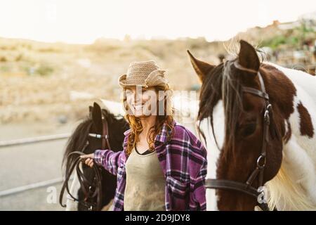 Junger lächelnder Bauer, der sich um die Pferde im Ranchstall kümmert Stockfoto