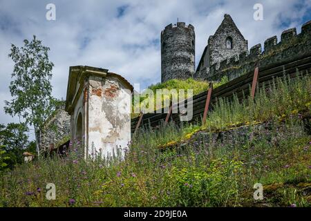 Bezdez, Tschechische Republik - Juli 19 2020: Blick auf eine Kapelle, einen Turm und ein Haus, Teile der mittelalterlichen Burg aus grauen Steinen auf einem grünen hil stehen Stockfoto
