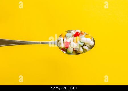 Löffel voller Pillen auf gelbem Hintergrund. Selbstmedikation und Drogenmissbrauch Konzept. Stockfoto