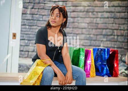 afroamerikanische Frau, die mit farbigen Einkaufstaschen im Einkaufszentrum sitzt. Stockfoto