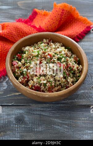Peruanischer Salat mit Quinoa, frischem Gemüse und Tomaten. Leckere gesunde vegetarische Speisen. In einer Holzschale auf einem Holzhintergrund, selektiver Fokus Stockfoto