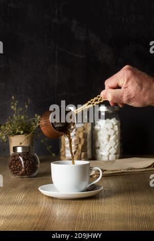 Mann, der einen türkischen Kaffee auf einem Holztisch serviert Ein dunkler Hintergrund Stockfoto