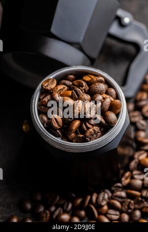 Kaffeebohnen und bialetti-Kaffeemaschine. Moka Topf auf schwarzem Tisch. Stockfoto