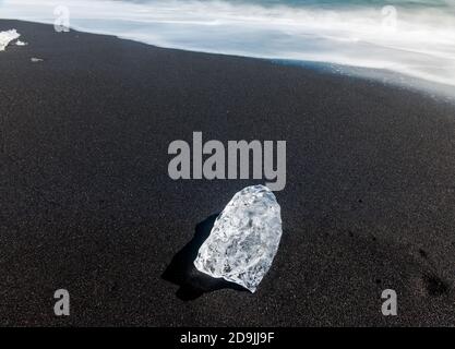 Schöner Strand im Süden Islands mit einem schwarzen Lavasand und einem einzigen Stück Eis. Mit einer langen Belichtung Stockfoto