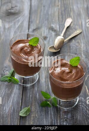Leckere vegane Schokoladenmousse mit Banane, Kakao und Minze in Gläsern auf Holzoberfläche, selektiver Fokus Stockfoto