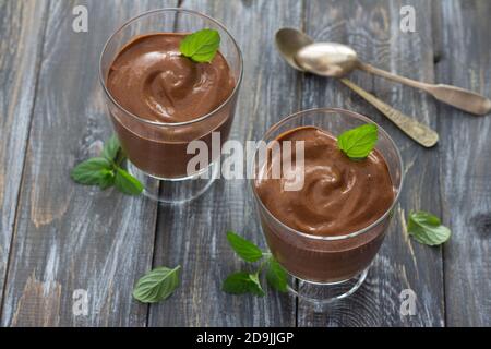 Leckere vegane Schokoladenmousse mit Banane, Kakao und Minze in Gläsern auf Holzoberfläche, selektiver Fokus Stockfoto