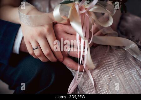 Die Hände der Braut und des Bräutigams mit den Eheringen und Blumenstrauß aus nächster Nähe Stockfoto