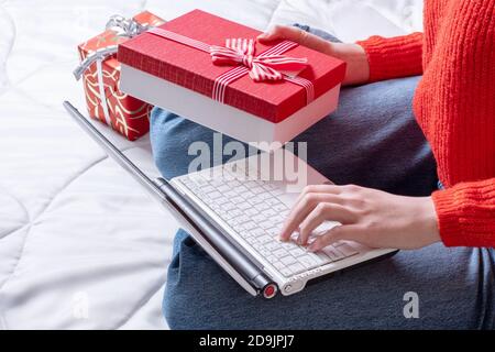 Draufsicht weibliche Hand hält eine Geschenkbox und macht Einkäufe auf einem Laptop. Frau kauft Geschenke, bereitet sich auf Weihnachten vor, Geschenkbox in der Hand. Winterurlaub Sal Stockfoto