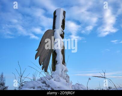 Totem geflügelte Holzskulptur bedeckt mit Schnee gegen den Himmel Stockfoto