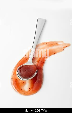 Gebogene Swinge und Löffel voll von pikanten Marmelade auf der Basis von pikant Soße in einem Werbe- oder Menükonzept auf Weiß Stockfoto