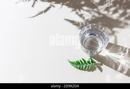 Glas von sauberem transparentem Wasser auf einem hellen Hintergrund in natürlichem Licht mit harten Schatten. Stockfoto