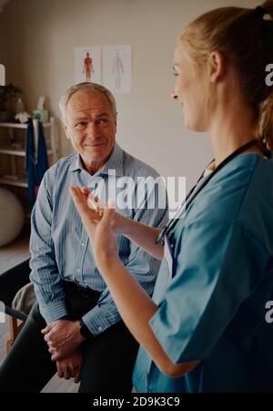 Glücklicher pensionierter Patient sititng in der Klinik Hören auf weibliche Ärztin Informationen zur Bestrahlung Stockfoto