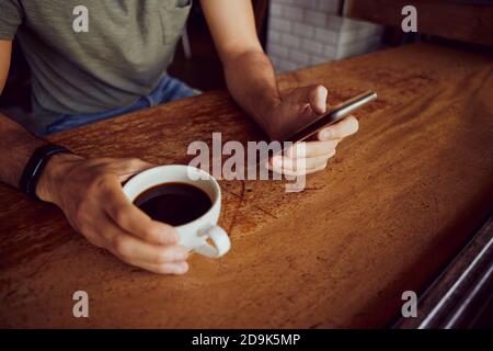 Nahaufnahme von männlichen Händen halten Telefon und Kaffeebecher während Sitzen und Entspannen im Café Stockfoto